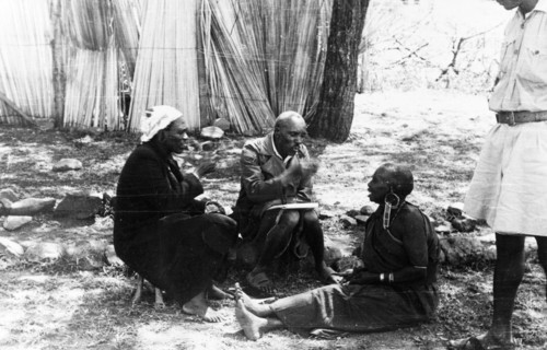 Interviewing a Mau Mau suspect. Two Kikuyu men gesticulate at an older Kikuyu woman seated on the