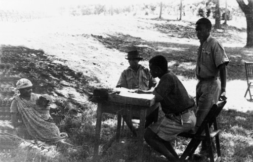 Questioning a Mau Mau suspect. Three men in lightweight uniforms question a Kikuyu woman with a