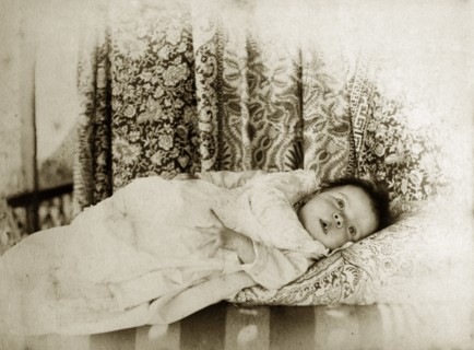 Portrait of a baby, Australia. A young baby dressed in a white gown gazes curiously into the