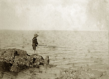 Young boy fishing, Australia. A lone boy wearing a sailor suit and hat, holds his fishing line out
