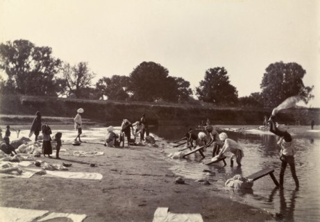 Washing day at the river. Washing clothes at the edge of a river. Several Indian men thrash and