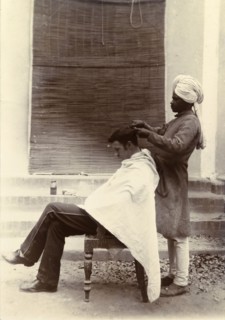 Cut your hair Sir'. A turbaned Indian barber trims the hair of a British gentleman who sits