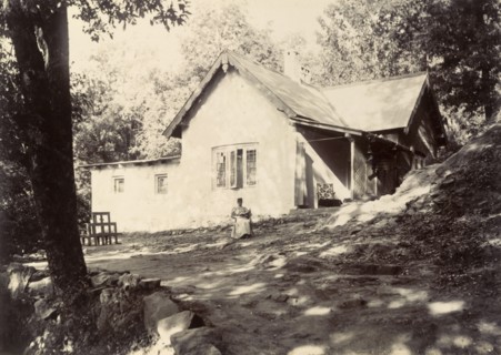 Mrs Page reads in the garden. A distant figure identified as 'Mrs Page' sits reading her book in