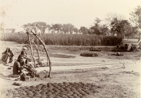Weaving in the fields. Indian weavers pause for a moment, crouched beside their hand looms. The