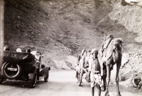 Road traffic near Suez. An Egyptian man leads a camel and cart along a winding road past a motorcar