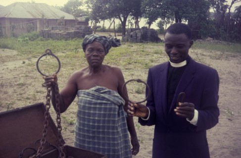 Slave chains at Badagry. A Nigerian woman and priest display metal chains that would once have been