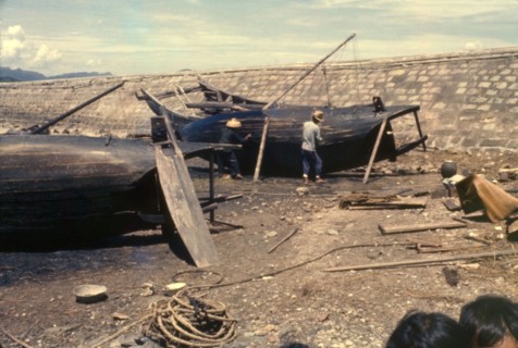 Re-caulking a sampan. Fishermen re-caulk the upturned bottoms of their sampans, filling in the