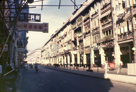 A street in Wan Chai. A row of tall shop buildings, littered with signs written in Chinese script,