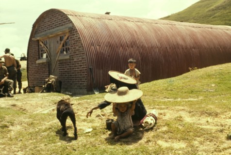 Container shed at Hebe Hill. A family sits on the ground outside a tubular-shaped container shed,