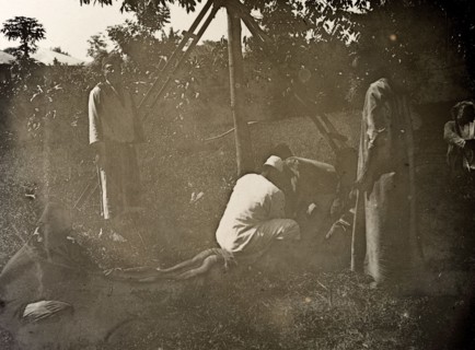 A young thief receives punishment. Several men restrain a thief, one sitting on his back as another