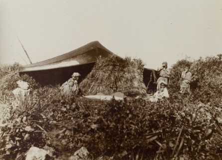 Temporary dwelling, Morocco. A group of people sit around a harvested bundle of straw outside a