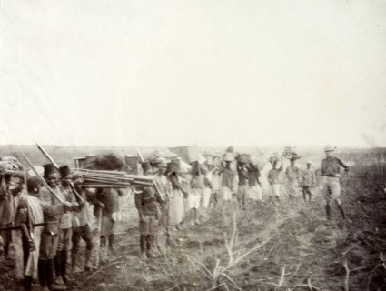 Frederick Stanbury bids farewell. A group of African porters and servants wait in line holding