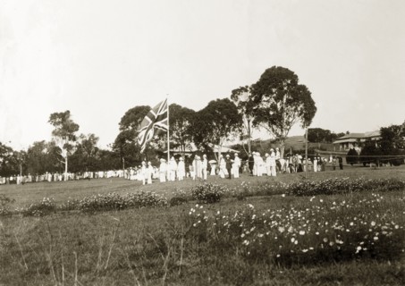 The King's birthday reception. A union jack flag, surrounded by men in white uniforms, flies high