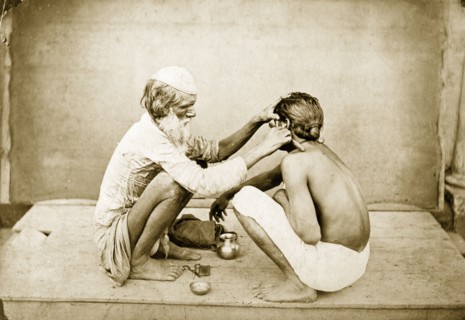 An Indian barber. An Indian barber crouches down on an outdoor platform as he shaves a customer's