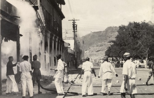 Relief work after the Arab riots in Aden, 1947. Teams of men use two hose pipes to douse the flames