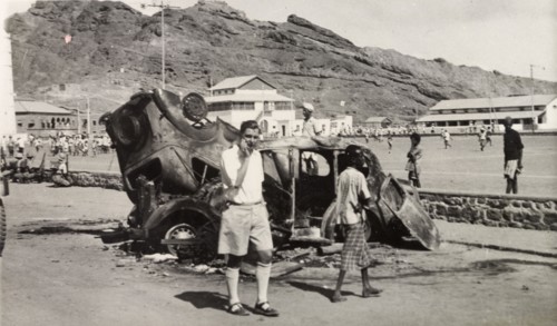 Vehicles destroyed during Arab riots in Aden, 1947. A European man stands by the burnt out shells