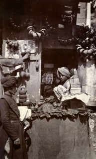 Roadside stall at Mussoorie bazaar. An Indian man sits hunched up on a roadside stall in a bazaar