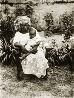 Mother and child, Nigeria. Portrait of a seated African woman holding a baby on her knee. She wears