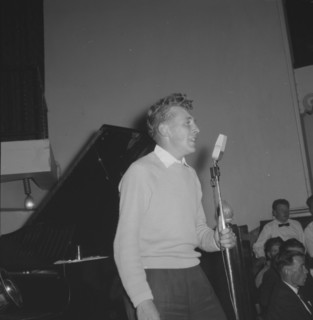 Jazz Ball singer. A casually dressed singer, supported by a band, clutches an upright microphone as