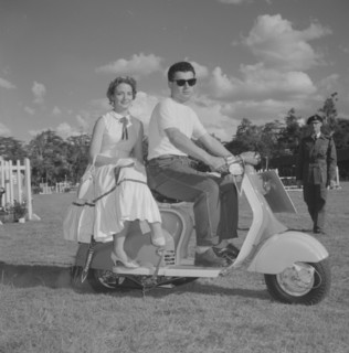 Couple on a scooter. A young couple in typical 1950s Western dress sit on a scooter in a vehicle