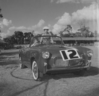 Number 12 on parade. A couple sit inside an open-top car marked with the number 12 at a vehicle