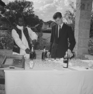 Wedding barmen. A young European man assists a uniformed African servant to pour champagne at the