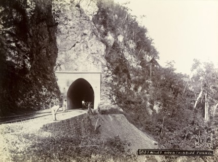 Mountainside tunnel, Jamaica. Three men stand at the entrance to a railway tunnel cut into the side