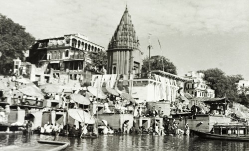 Hindu temple at Benares. Religious pilgrims sit beneath large umbrellas at a ghat (stepped wharf)