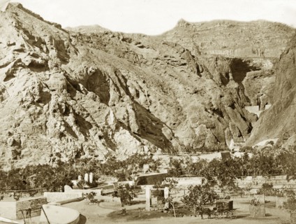 Water wells, Aden. Steep mountains rise up immediately behind several masonry wells, which are