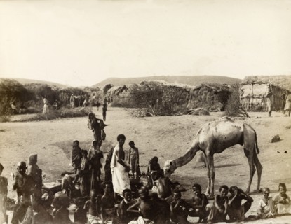 Village scene at Aden. A cluster of people, many of them children, stand or squat on the sand in