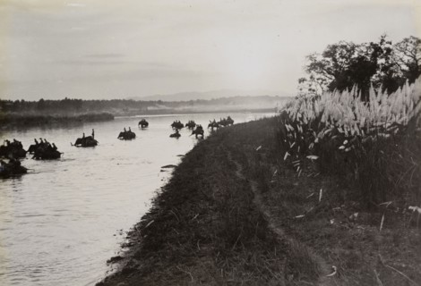 Return to camp. Mounted on elephants, King George V's royal hunting party crosses a river at sunset