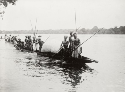 Canoes near Kandahar Island. A group of semi-naked men wearing traditional dress and headgear,
