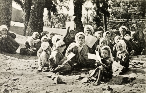 Outdoors school, Egypt. A group of young children sit cross-legged on a patch of desert sand as