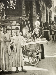 Street peddler, Cairo. A street peddler sells food from a cart whilst two boys in traditional dress