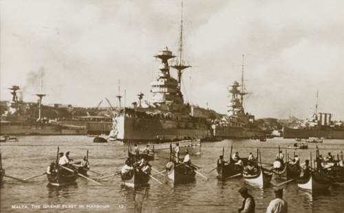 The Grand Fleet at Malta. Several small luzzus (row boats) share a Maltese harbour with two huge