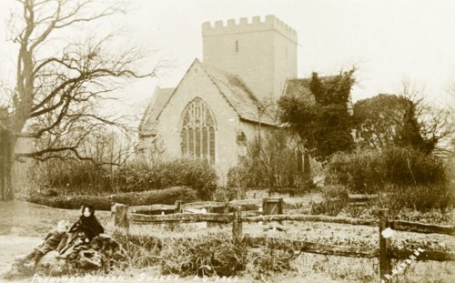 Holy Trinity Church, Poynings. Two small children sit on a log outside Holy Trinity Church.