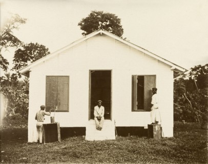 Painting the shutters. Two men paint shutters on the exterior of a small building with a pitched