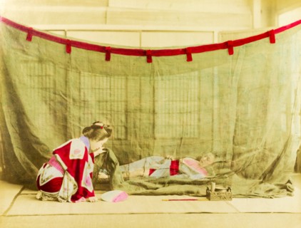Japanese sleeping arrangements. A kneeling Japanese woman dressed in a kimono lifts the corner of a