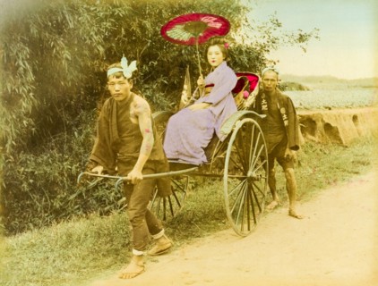A Japanese rickshaw. A young Japanese woman travels along a rural road in an open rickshaw pulled