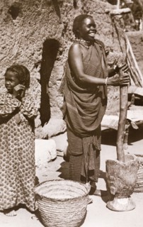 Grinding 'durra', Sudan. A Sudanese woman in traditional dress smiles as she uses a large pestle