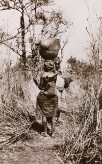 How women travel in the Sudan'. Two Sudanese women in traditional dress walk along an overgrown