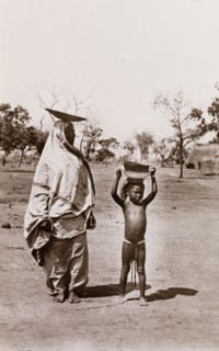 Mother and child carrying bowls. A mother and her child carry bowls on their heads along a village