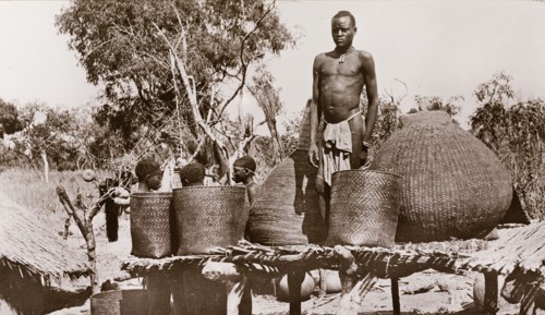 A village granary, Sudan. A man in a loincloth stands on a raised platform between several baskets