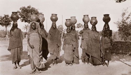 Sudanese women carrying water. A group of Sudanese women, dressed in long robes and headscarves,