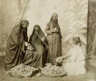 North African apple seller. Posed studio portrait of a man wearing a fez selling apples to three