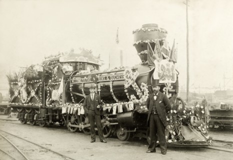 Royal train at Perth. Two men stand beside a locomotive, decorated with flowers and bunting for the