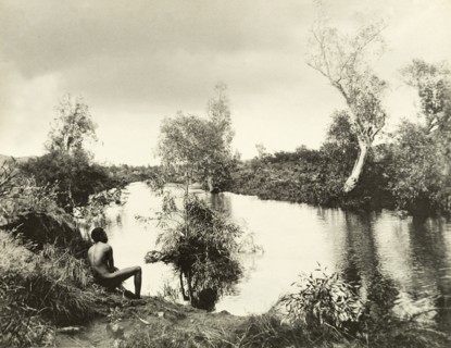 An aborigine on the banks of a backwater. An aborigine sits with his back to the camera on the