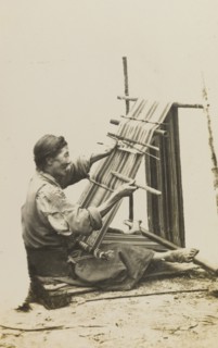 Bhatia woman weaving cloth. An elderly Bhatia woman sits on the ground, operating a frame loom by