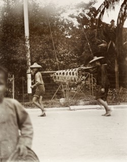 Usual method of carrying a pig'. Two Chinese men carry a pig in a wicker cage suspended from a pole