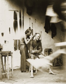Ear cleaning at a barber's shop, China. A man with a distinctive Manchu hairstyle sits on a stool